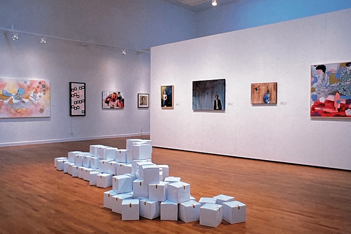 an art display of white blocks stacked with art hanging off a wall behind it.